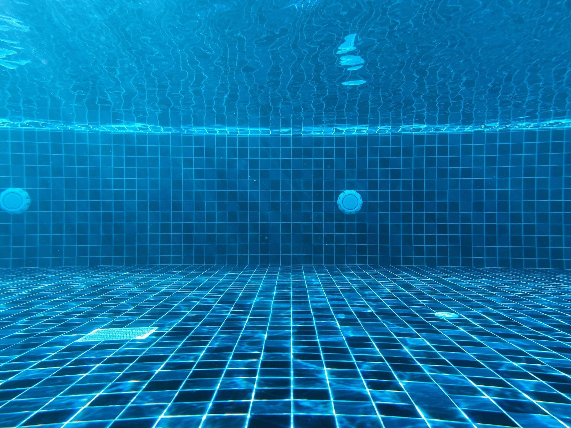Underwater view of a blue tiled pool floor and drain